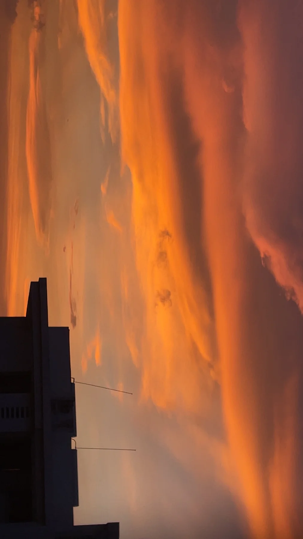 Orange sunset clouds above the dark silhouette of a rooftop, photographed in a sideways composition.