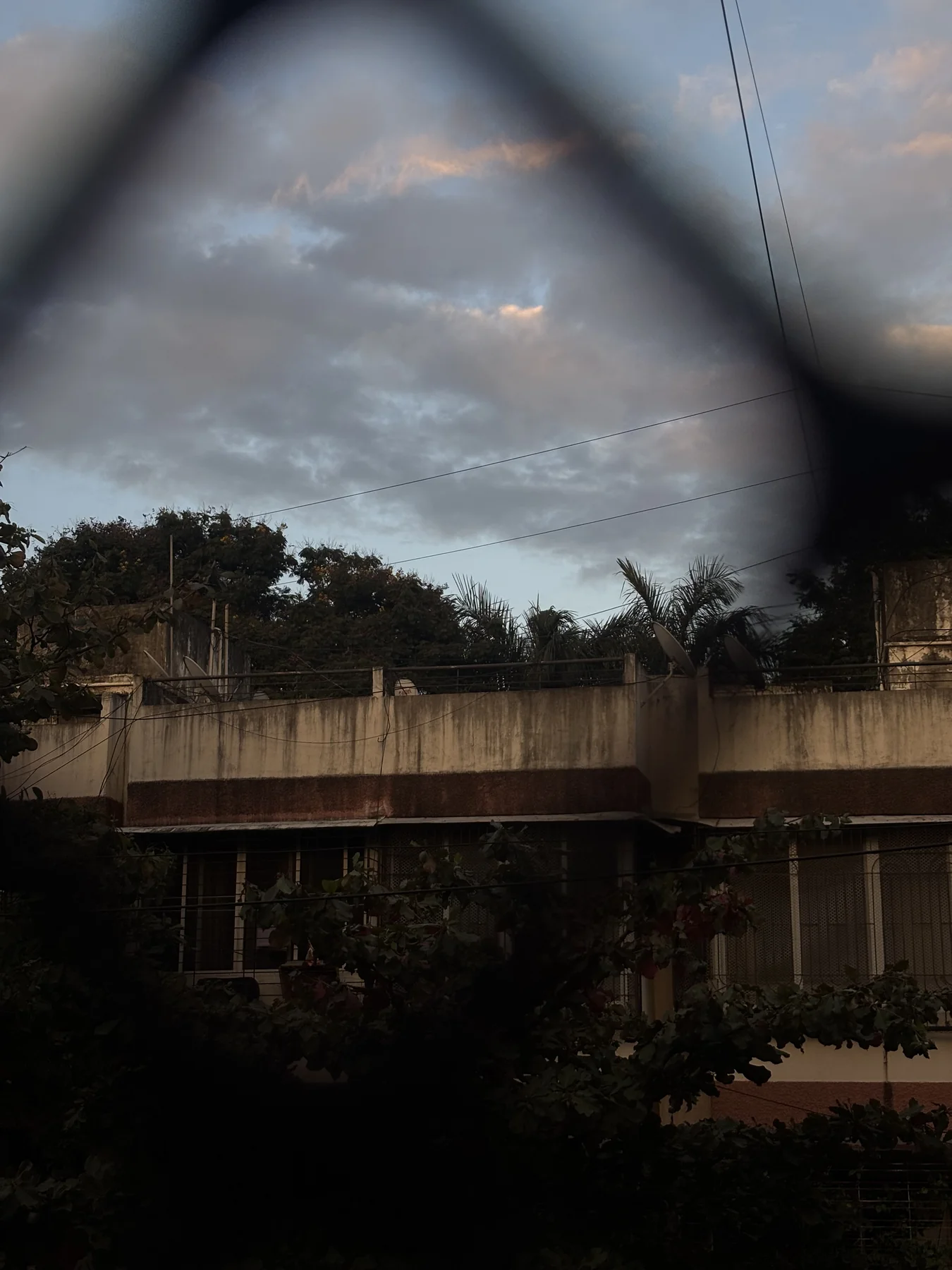 A moody evening sky and an older building seen through an out-of-focus wire fence.
